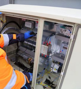 Engineer in safety gear working on an outdoor electrical panel, ensuring system functionality.